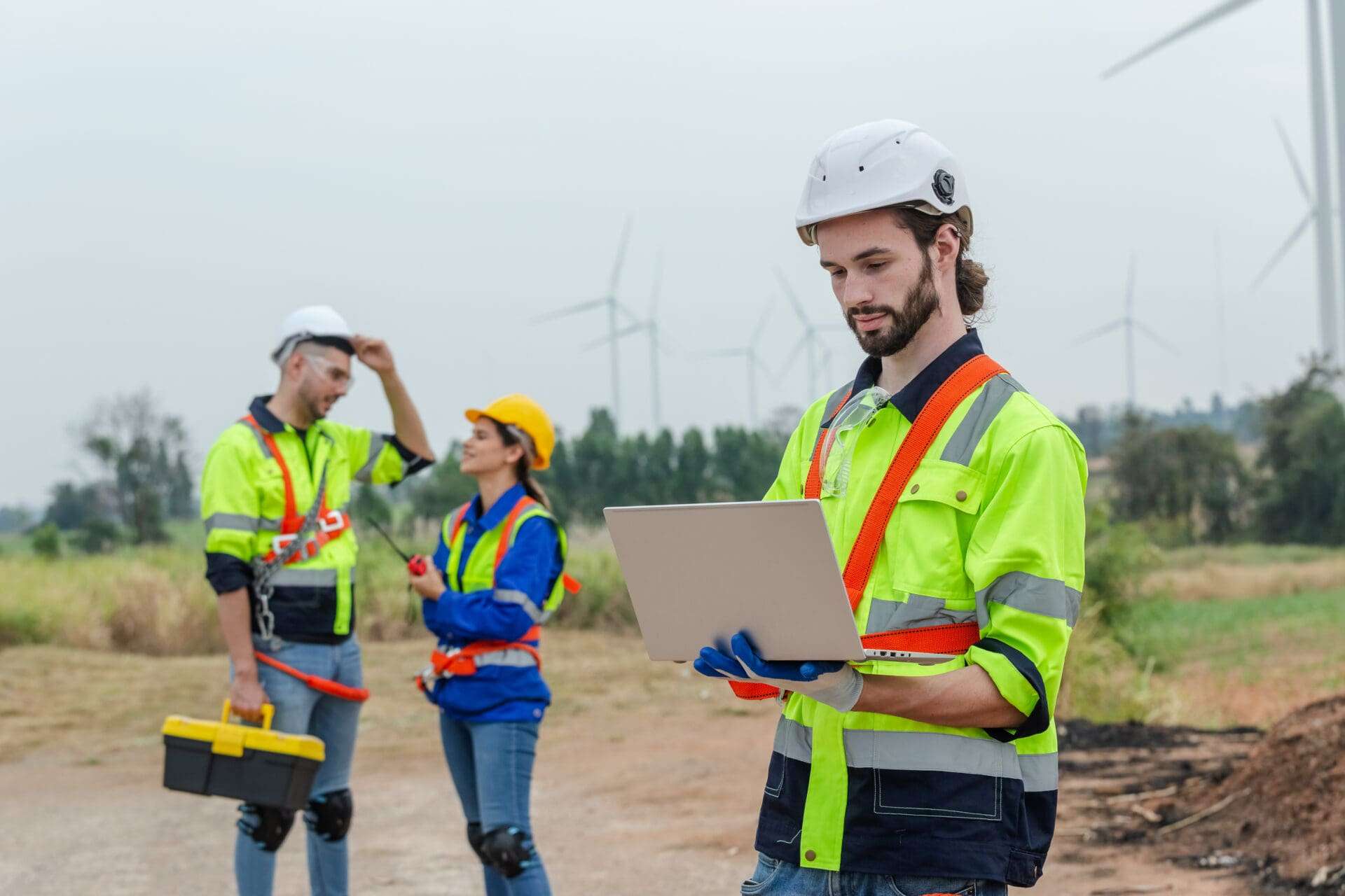 Team engineer using laptop on worksite while two colleagues stand in background.