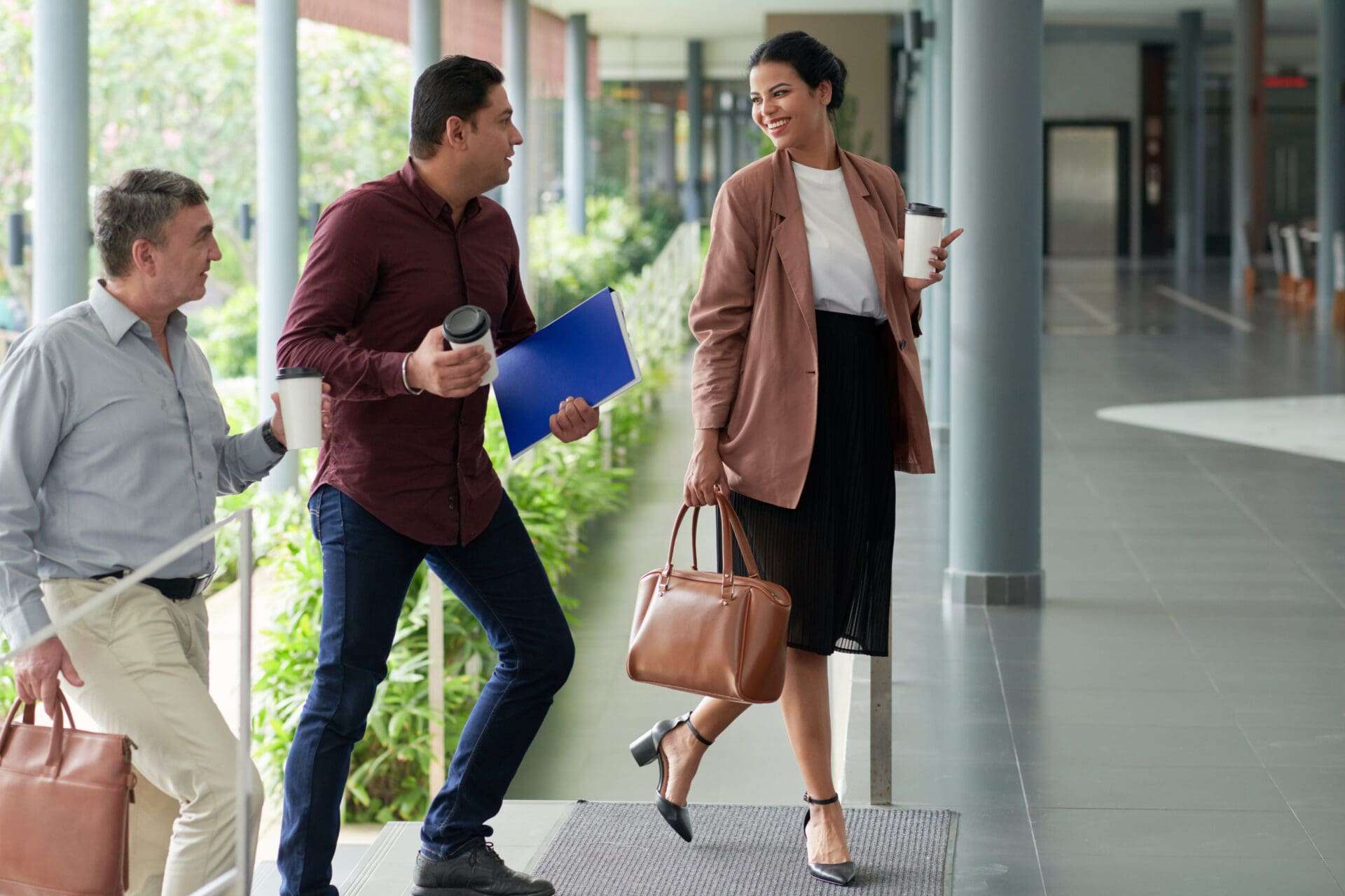 Smiling elegant woman with cup of coffee and her colleagues entering the office