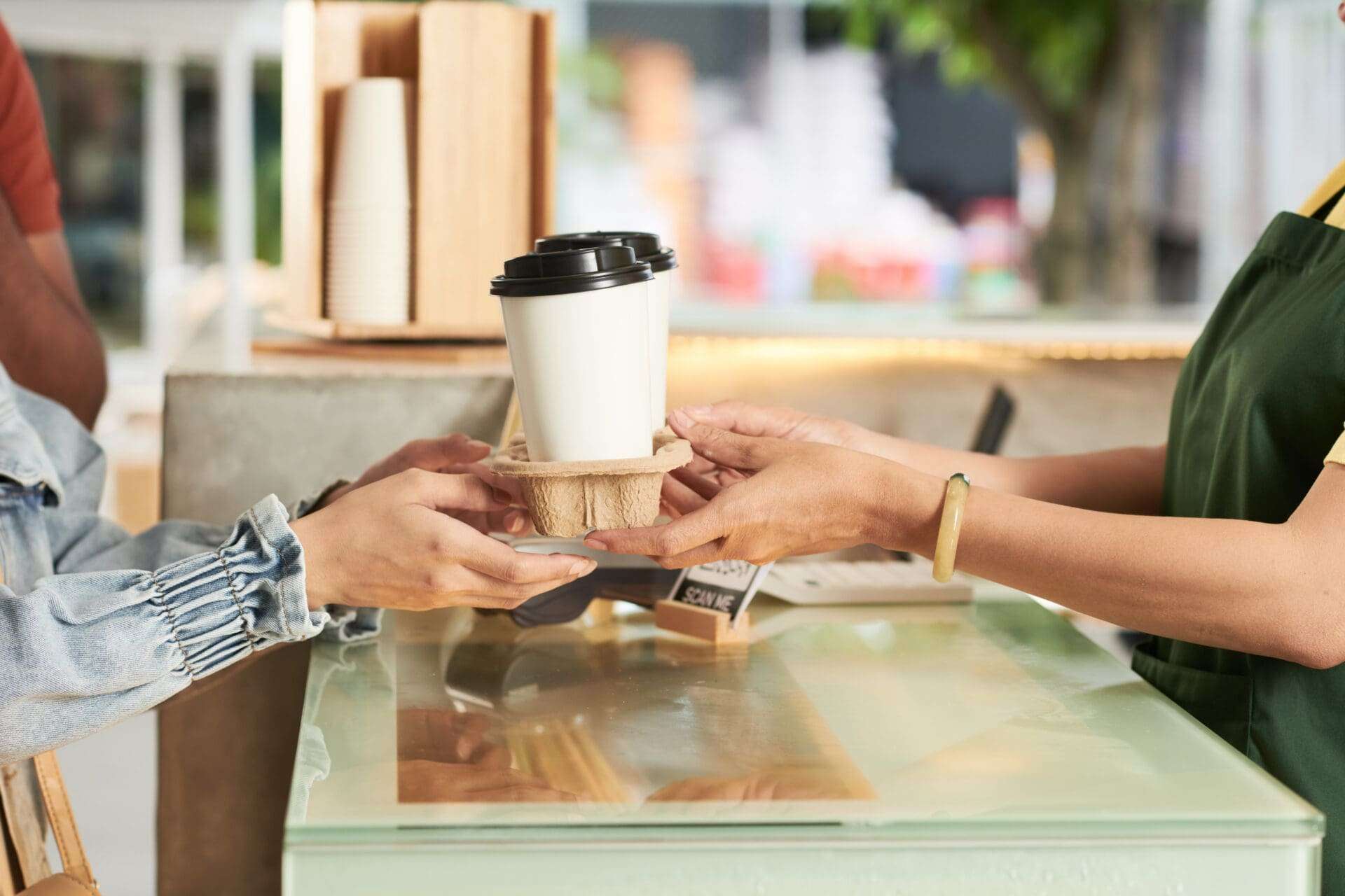 Hands of a barista and customer buying take out coffee in cafe