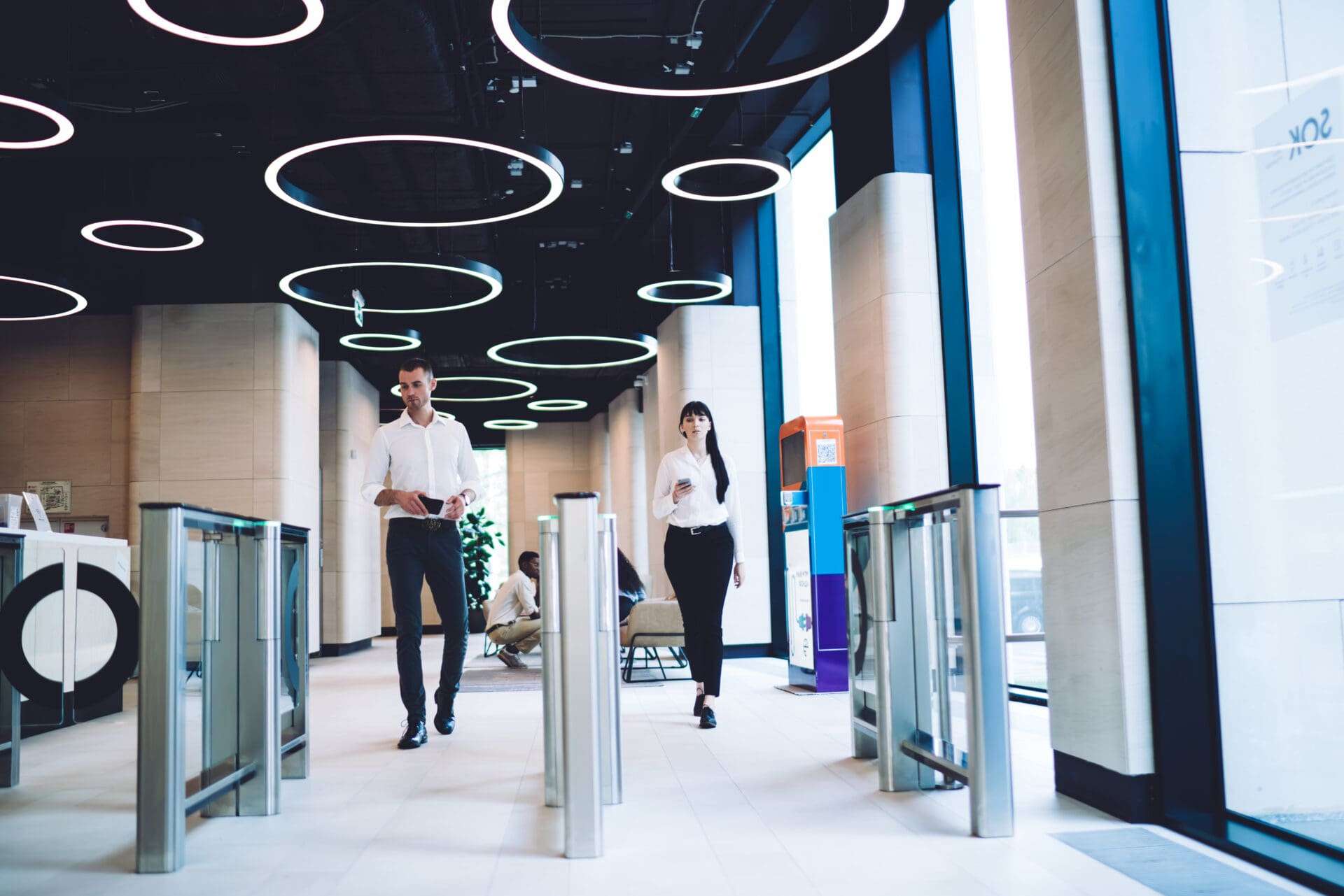 Calm smart colleagues in trendy formal wear going through automatic turnstile gates in hall of light modern building